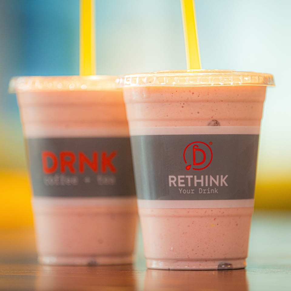 Two Qwench Juice Bar smoothies with yellow straws on a wooden surface.