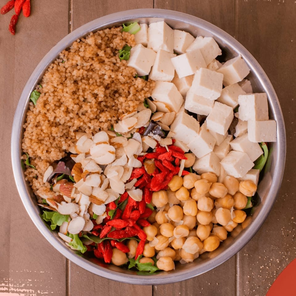 Overhead view of a Qwench Juice Bar salad with quinoa, tofu, almonds, goji berries, and chickpeas.