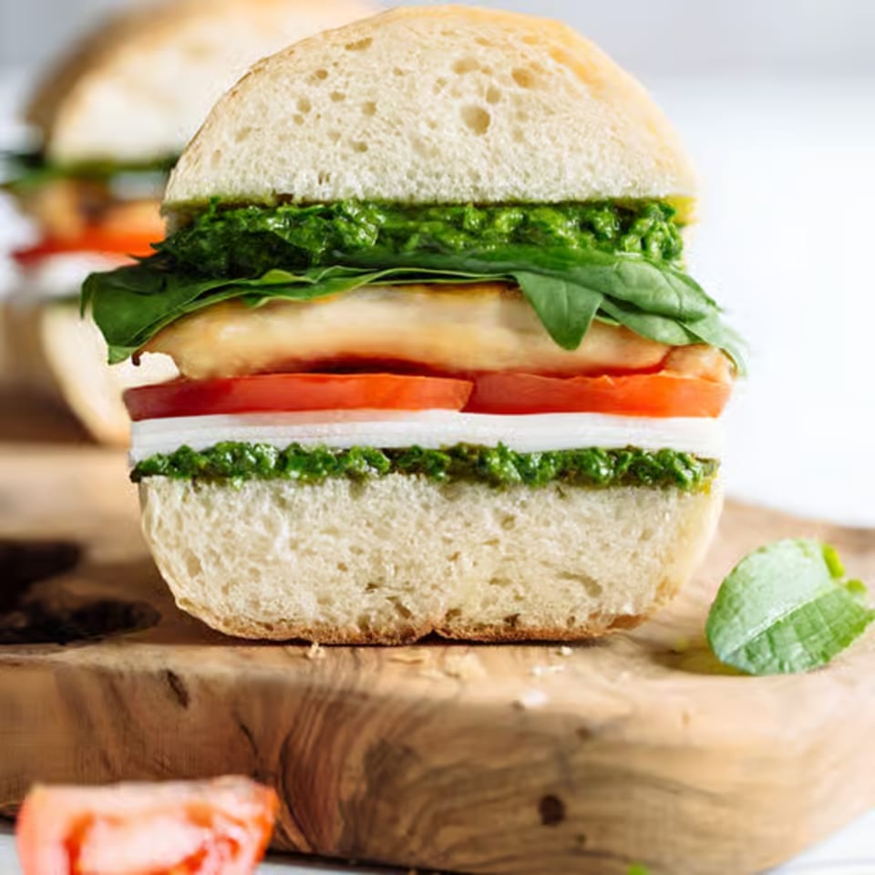 A close-up of a sandwich with pesto, mozzarella, tomato, and chicken on a wooden board.