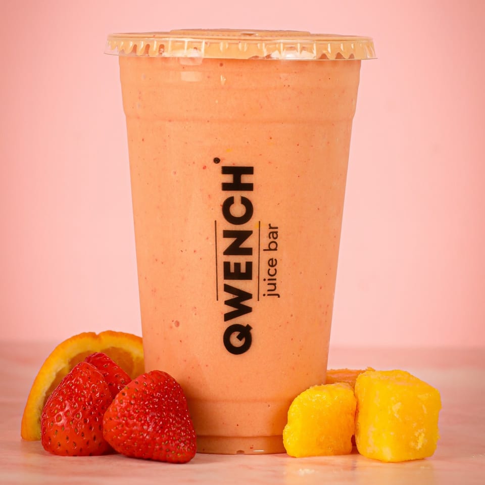Qwench Juice Bar smoothie with strawberries, orange slice, and mango chunks on a pink background.